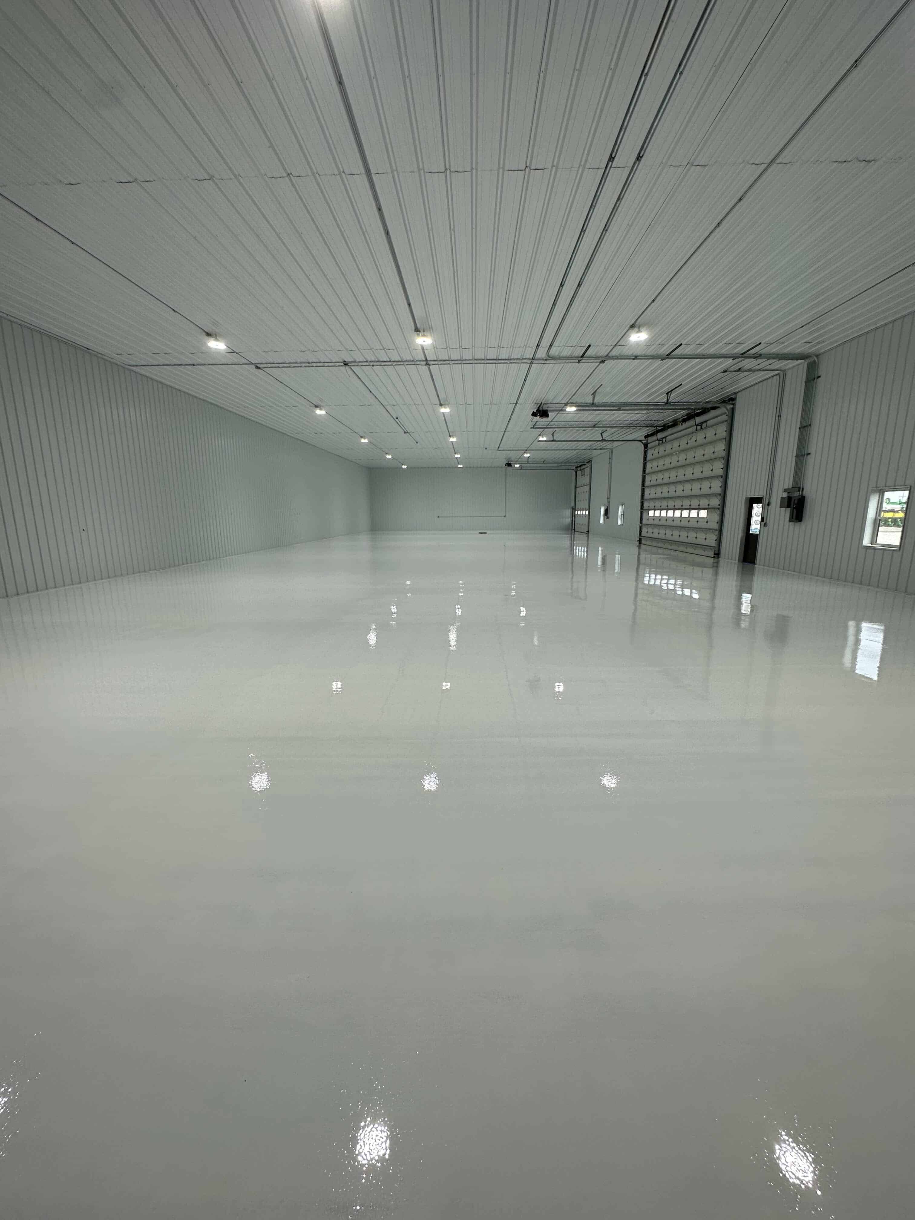 High-gloss poured epoxy floor reflecting the lights of a finished industrial warehouse — a Salyers Construction coating