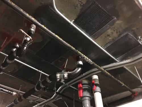Carbon fiber strengthening bonded to an overhead concrete beam amid process piping in an industrial plant
